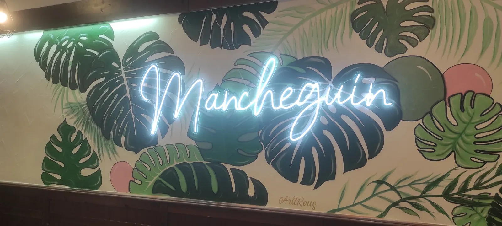 Rótulo de neón LED con el nombre de un bar sobre una pared pintada con hojas de monstera